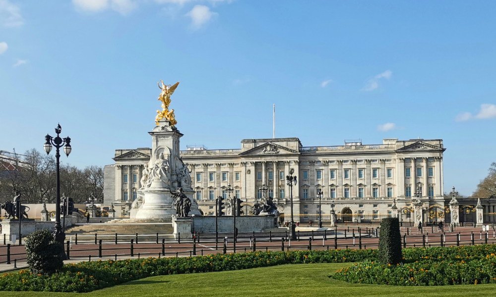 Front view of Buckingham Palace in London, showing its grand façade and the forecourt with a few visitors.