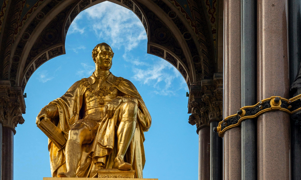 The Albert Memorial statue in Kensington Gardens, London, with its golden figure and ornate detailing, surrounded by greenery.
