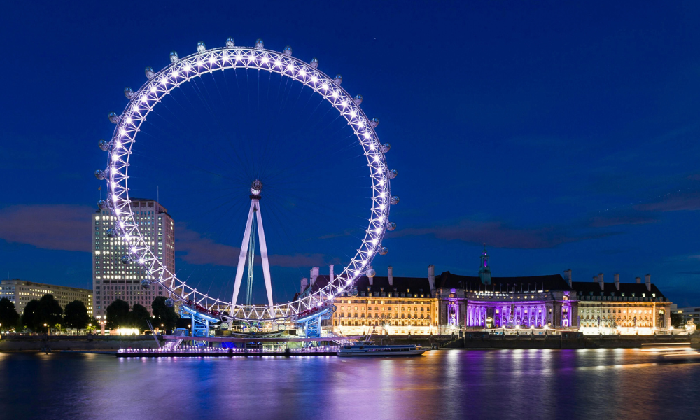The London Eye Ferris wheel on the South Bank of the Thames in London, with the river and city skyline in the background.
